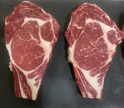 Two thick cuts of ribeye steak displayed on a black cutting board, showcasing marbling and rich red color, ideal for grilling or pan-searing.
